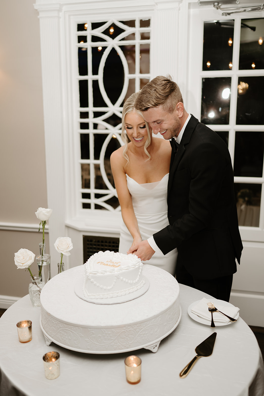 Bride and groom smile as they cut a heart-shaped wedding cake together during their reception.